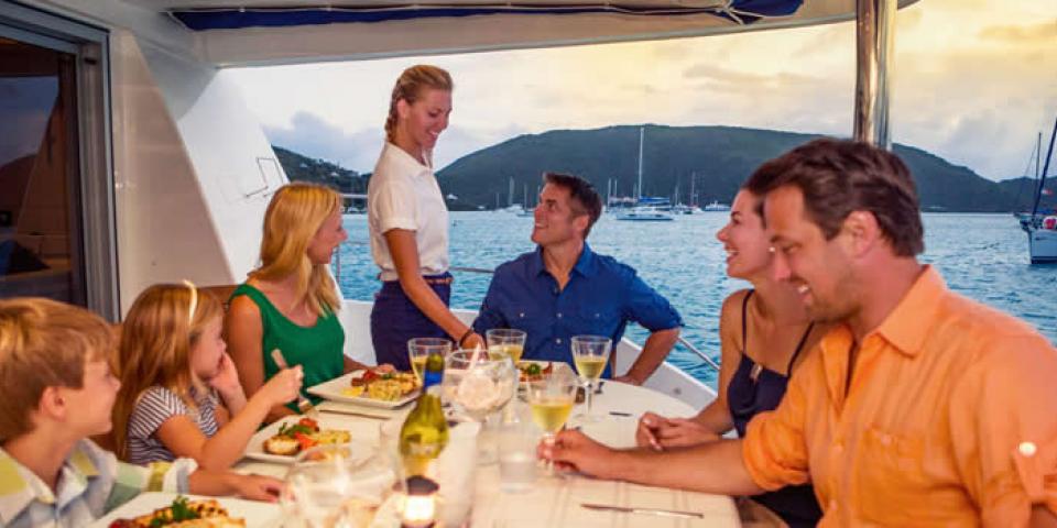 Hostess serving wine as a family sits down to a meal on a crewed yacht in the British Virgin Islands.